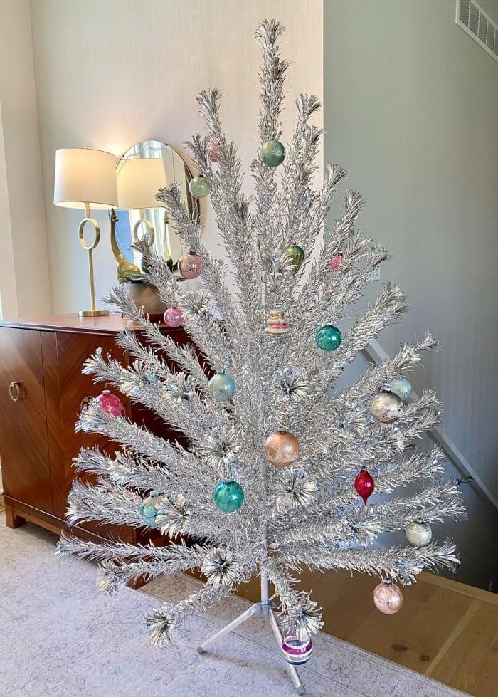 An Evergleam 94-branch stainless aluminum six-foot Christmas tree with tripod stand, 1960s, by Aluminum Specialty of Manitowoc, Wisconsin. The Shiny Brite ornaments shown on tree were not included with the sale; $500.